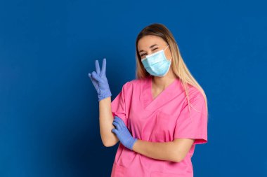 Maske takan genç bir doktor ve mavi arka planda pembe üniformalı.