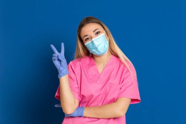 Maske takan genç bir doktor ve mavi arka planda pembe üniformalı.