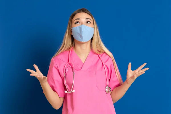 Junger Arzt Mit Maskengesicht Und Rosa Uniform Auf Blauem Hintergrund — Stockfoto