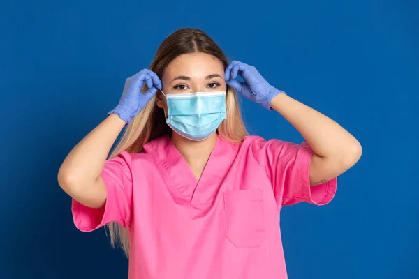 Jovem Médico Vestindo Rosto Máscara Uniforme Rosa Fundo Azul — Fotografia de Stock