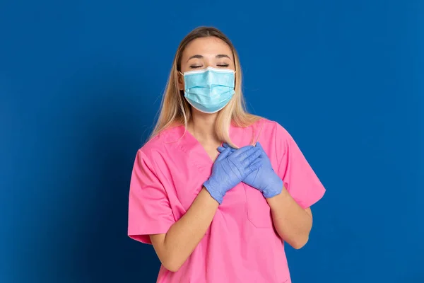 年轻医生 戴着面具 身穿蓝色背景的粉色制服 — 图库照片