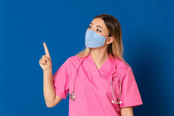 年轻医生 戴着面具 身穿蓝色背景的粉色制服 — 图库照片