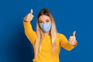 Mavi arka planda maske takan sarışın kız.