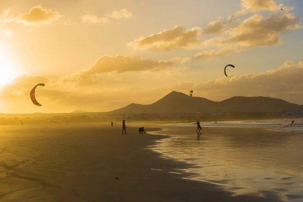 scenic view of people walking and kiting on beach at sunset