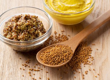 İki hardal sosu ve hardal tohumunun çapraz görünümü ahşap bir zemine yerleştirilmiş.