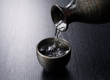 Siyah bir fonda sake bardağına sake dökmek