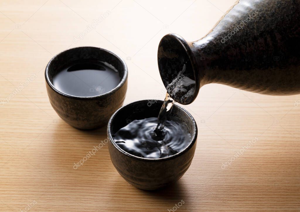 Pouring sake into a sake cup set against a wooden backdrop