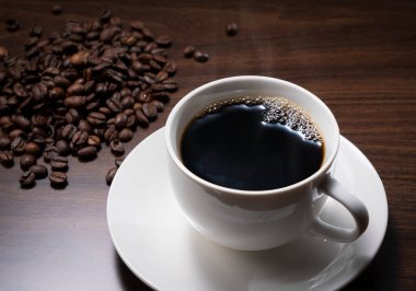 Koyu bir ahşap zemine karşı sıcak kahve ve kahve çekirdekleri.