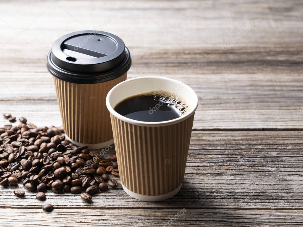 A paper cup of coffee and coffee beans on an old wooden background