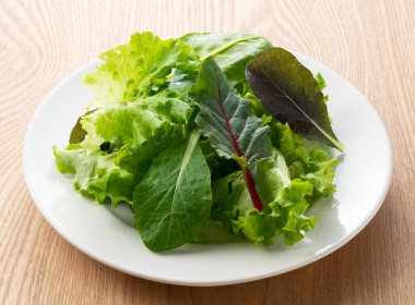 Tabaktaki çeşitli salata yaprakları ahşap arka planda.