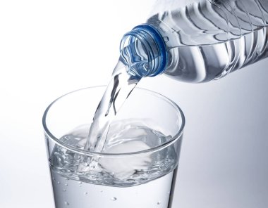 Beyaz arka plana yerleştirilmiş temiz bir bardağa şişe suyu dök..