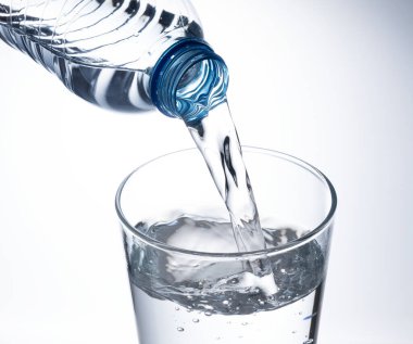 Beyaz arka plana yerleştirilmiş temiz bir bardağa şişe suyu dök..