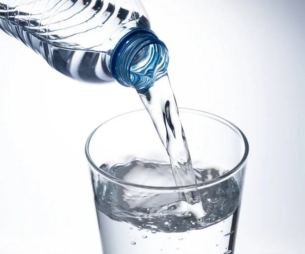 Beyaz arka plana yerleştirilmiş temiz bir bardağa şişe suyu dök..