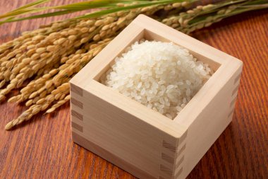 Rice and ears of rice in a Japanese Masu box set against a wooden background clipart