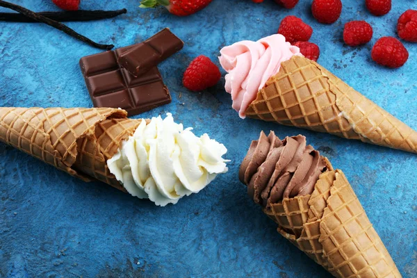 Vanilla frozen yogurt or soft ice cream in waffle cone and strawberry, raspberry and chocolate softice cream
