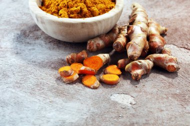 Zerdeçal tozu ve gri arka plan üzerinde taze zerdeçal.