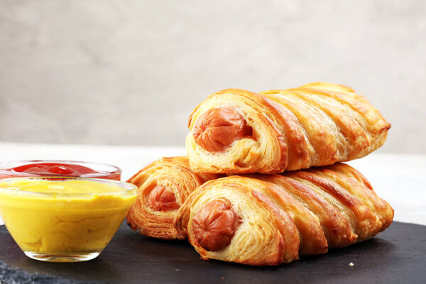 Вкусные домашние колбасные роллы на черном блюде
.