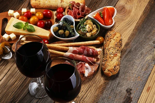İtalyan antipasti şarap aperatifler küme. Peynir çeşitli, Akdeniz zeytin, crudo, Prosciutto di Parma, salam ve ahşap grunge arka plan üzerinde bardaklarda şarap