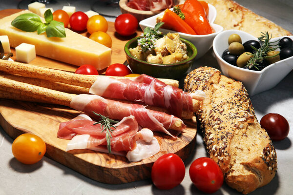 Italian antipasti wine snacks set. Cheese variety, Mediterranean olives, crudo, Prosciutto di Parma, salami and wine in glasses over stone grunge background