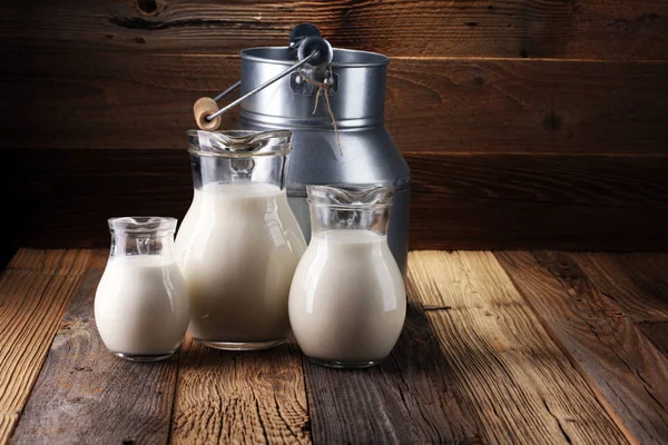 Um jarro de leite e copo de leite em uma mesa de madeira — Fotografia de Stock