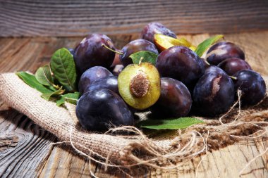 Erik rustik arka plan üzerinde. Mavi erik meyve yarısı. Yaprakları ile birçok güzel Erik.