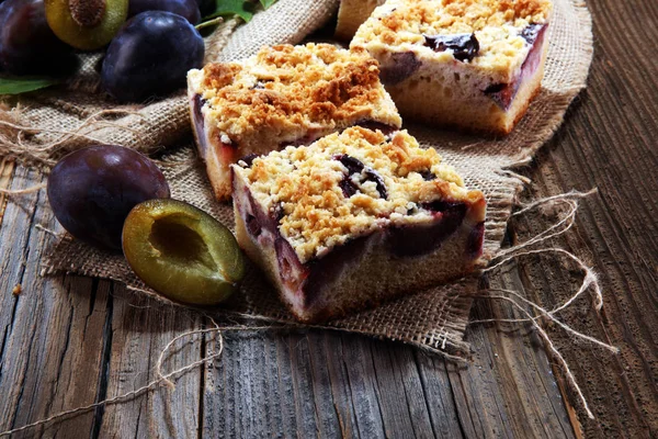 Rustic plum cake on wooden background with plums around