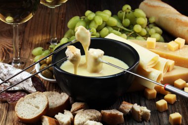 Bir kış akşamında gurme İsviçre fondü yemek peynir fondü iki çatal bir lokali veya restoran arkasında ekmek ve beyaz şarap daldırma ile ısıtmalı bir sürahi yanında bir gemide çeşitli peynir ile