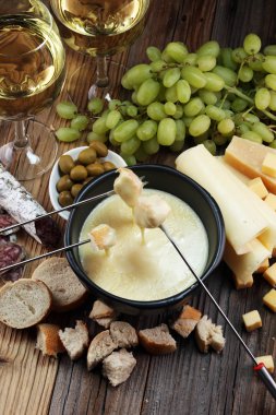 Bir kış akşamında gurme İsviçre fondü yemek peynir fondü iki çatal bir lokali veya restoran arkasında ekmek ve beyaz şarap daldırma ile ısıtmalı bir sürahi yanında bir gemide çeşitli peynir ile