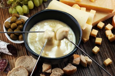 Bir kış akşamında gurme İsviçre fondü yemek peynir fondü iki çatal bir lokali veya restoran arkasında ekmek ve beyaz şarap daldırma ile ısıtmalı bir sürahi yanında bir gemide çeşitli peynir ile