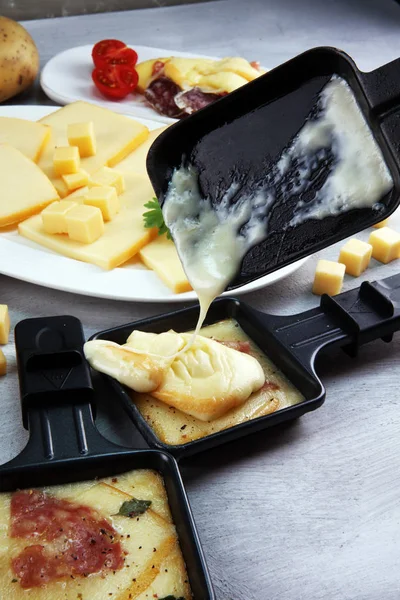 Delicious traditional Swiss melted raclette cheese on diced boiled or baked potato served in individual skillets with salami.