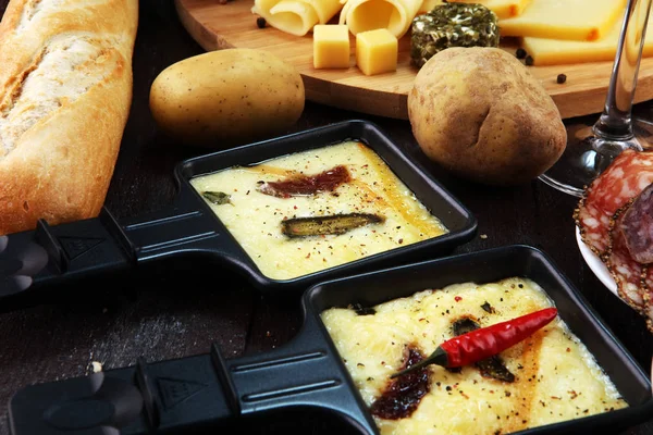 美味的传统瑞士融化 Raclette 芝士在煮熟或烤马铃薯在单独的煎锅与意大利腊肠服务 — 图库照片