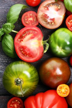 Kırsal masada çeşitli renkli domatesler ve fesleğen yaprakları. Taze zebra domates ve cccor de boeuf