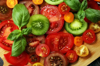 Kırsal masada çeşitli renkli domatesler ve fesleğen yaprakları. Taze zebra domates ve cccor de boeuf