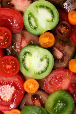 Kırsal masada çeşitli renkli domatesler ve fesleğen yaprakları. Taze zebra domates ve cccor de boeuf