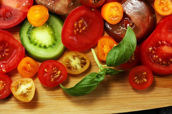 Kırsal masada çeşitli renkli domatesler ve fesleğen yaprakları. Taze zebra domates ve cccor de boeuf