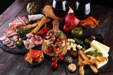 İtalyan antipasti şarap aperatifler küme. Peynir çeşitli, Akdeniz zeytin, turşu, Prosciutto di Parma, domates, enginar ve şarap gözlük siyah grunge arka plan üzerinde