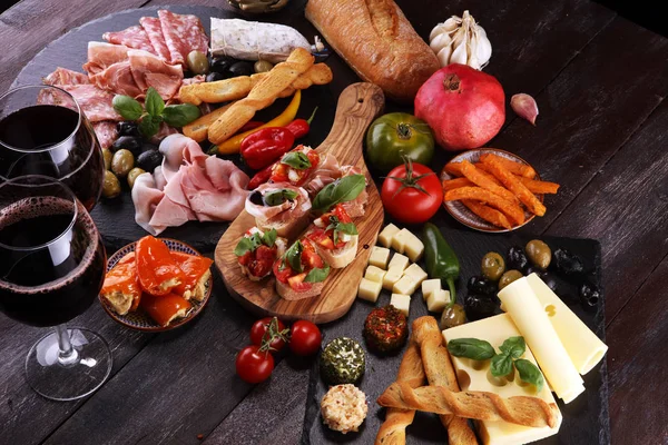 İtalyan antipasti şarap aperatifler küme. Peynir çeşitli, Akdeniz zeytin, turşu, Prosciutto di Parma, domates, enginar ve şarap gözlük siyah grunge arka plan üzerinde