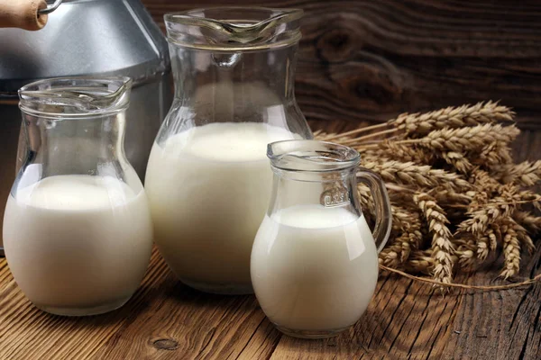 A jug of milk and glass of milk on a wooden table.