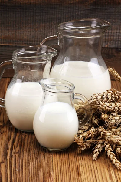 A jug of milk and glass of milk on a wooden table.