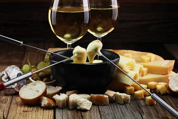 Bir kış akşamında gurme İsviçre fondü yemek peynir fondü iki çatal bir lokali veya restoran arkasında ekmek ve beyaz şarap daldırma ile ısıtmalı bir sürahi yanında bir gemide çeşitli peynir ile