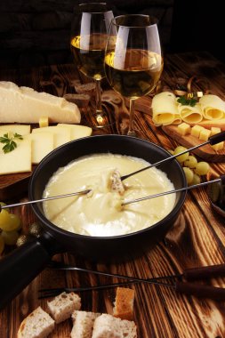 Bir kış akşamında gurme İsviçre fondü yemek peynir fondü iki çatal bir lokali veya restoran arkasında ekmek ve beyaz şarap daldırma ile ısıtmalı bir sürahi yanında bir gemide çeşitli peynir ile