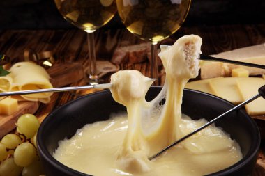 Bir kış akşamında gurme İsviçre fondü yemek peynir fondü iki çatal bir lokali veya restoran arkasında ekmek ve beyaz şarap daldırma ile ısıtmalı bir sürahi yanında bir gemide çeşitli peynir ile