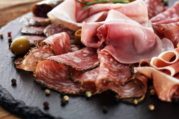 Marble cutting board with prosciutto, bacon, salami and sausages on wooden background. Meat platter