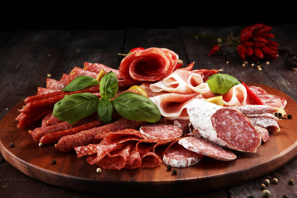Food tray with delicious salami, pieces of sliced prosciutto crudo, sausage and basil. Meat platter with selection.