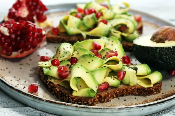 sliced avocado and ripe pomegranates on toast bread with spices and avocado