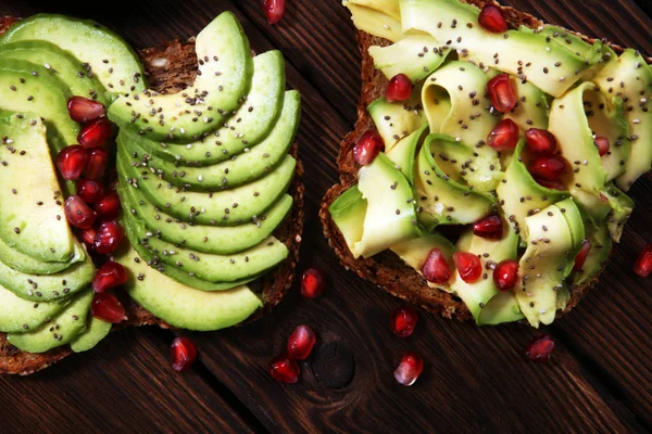 sliced avocado and ripe pomegranates on toast bread with spices and avocado