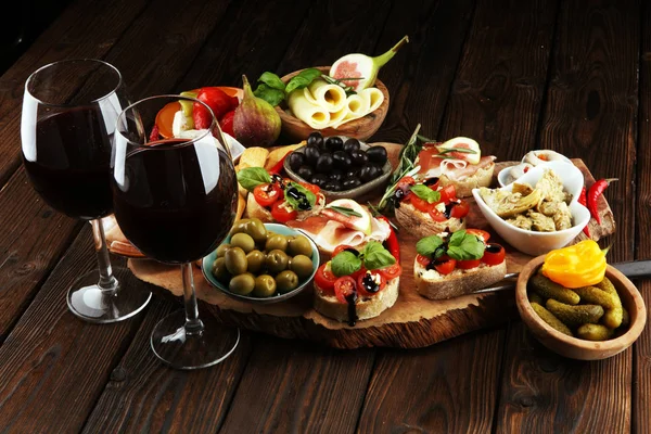 İtalyan antipasti şarap aperatifler küme. Peynir çeşitli, Akdeniz zeytin, turşu, Prosciutto di Parma, domates, enginar ve masada bardaklarda şarap