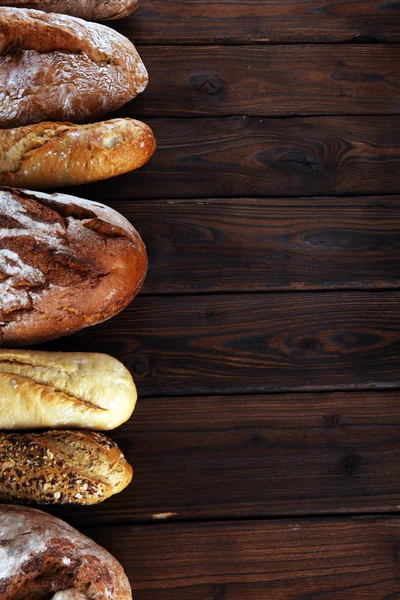 Assortment of baked bread and bread rolls on wooden table background. Bakery poster concept