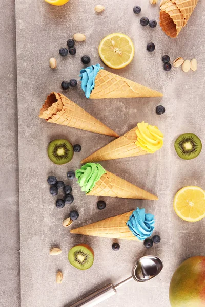Vanilla frozen yogurt or soft ice cream in waffle cone. Diffrent flavor ice cream with kiwi and pistachio, mango and lemon, blueberry and blackberry