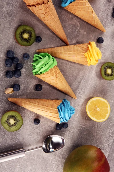 Vanilla frozen yogurt or soft ice cream in waffle cone. Diffrent flavor ice cream with kiwi and pistachio, mango and lemon, blueberry and blackberry